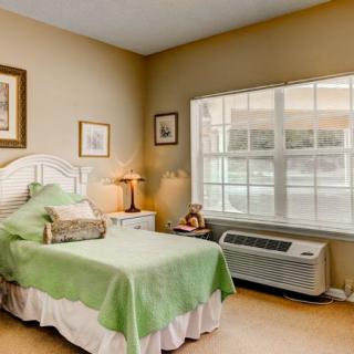 A cozy bedroom with a green bedspread, framed artwork, and large windows.