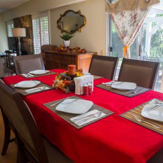 A dining room table set with a red tablecloth, ready for a holiday meal.