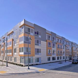 A modern multi-story apartment building featuring a blend of materials and design elements against a clear blue sky.