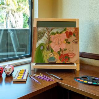 A colorful painting on an easel by the window, surrounded by art supplies including colored pencils and a palette.