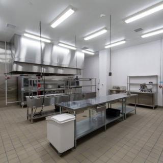 An empty industrial kitchen with stainless steel workstations and appliances.