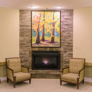 A cozy living room with a fireplace, flanked by two patterned chairs and a vibrant painting above.