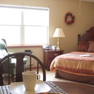 A cozy bedroom with a neatly made bed, a nightstand with a lamp, and a table set up for coffee.