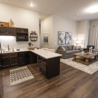A modern open floor plan featuring a kitchen with dark cabinetry and an island countertop, adjacent to a cozy living room area with stylish furniture.
