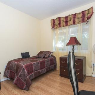 A cozy bedroom featuring a single bed, small desk with a lamp, and a window adorned with patterned curtains.