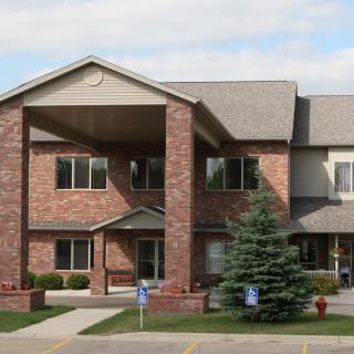 A two-story brick residential building with a pitched roof and a tree in front.