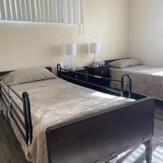 A room with two single beds, one of which is a hospital-style bed, in a healthcare or nursing facility.