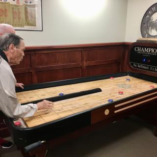 Two people playing a game of shuffleboard indoors.