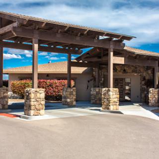 A modern entrance of a building featuring a wooden pergola and stone pillars, surrounded by well-maintained landscaping.