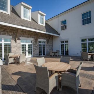 A sunny patio area with tables and chairs in front of a building.