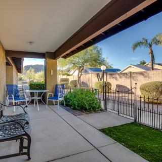 A sunny residential patio with chairs and a table, overlooking a garden and fenced yard.