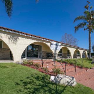 A long building with arched architecture and a manicured lawn, accented by palm trees under a clear blue sky.