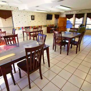 A spacious and empty dining area with wooden tables and chairs, featuring tiled flooring and natural light coming in.