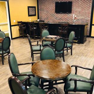 Cozy indoor lounge with tables and chairs, featuring a bar and television on a brick-accented wall.