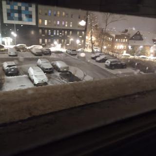 A view of a snowy parking lot at night, illuminated by city lights.