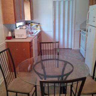 A compact kitchen and dining area featuring a glass table with four chairs, wooden cabinets, and various appliances.