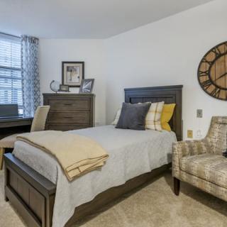 A cozy bedroom with a single bed, decorative pillows, and a wall clock.