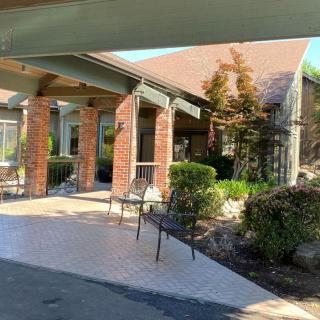 A sunny day view of a building entrance with chairs and landscaping.