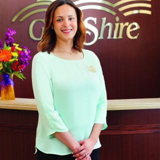 A woman stands in a professional reception area, smiling for the camera.