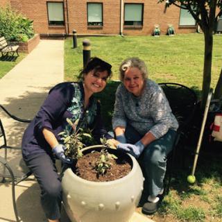 Two women enjoying a sunny day while planting flowers in a pot, bringing life to their community space.