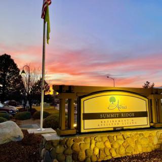 A beautifully lit sign at sunset, with a flag and buildings in the background.