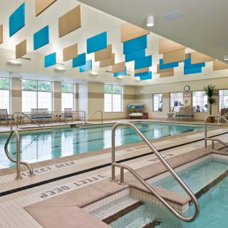 A modern indoor swimming and hydrotherapy pool area with bright lighting and decorative ceiling panels.