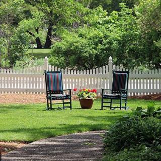 A peaceful backyard garden with two chairs facing each other next to a white picket fence.