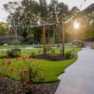 A beautifully landscaped garden at sunset with string lights and vibrant flowers lining a winding pathway.