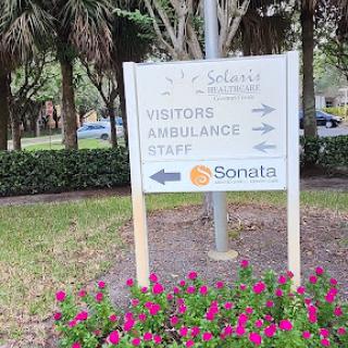 A directional sign indicating paths for visitors, ambulances, and staff, surrounded by blooming flowers.