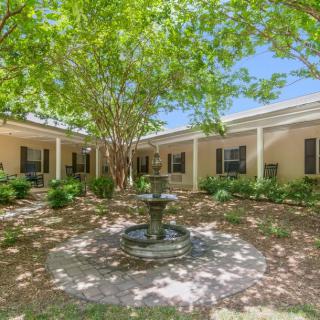 A serene courtyard featuring a central fountain surrounded by lush trees and a building with large windows.