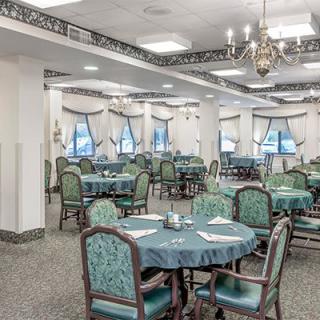 An elegant dining area with multiple tables set for guests, featuring traditional decor and a chandelier.