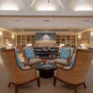 A cozy living room with large armchairs arranged around a coffee table, surrounded by bookshelves and warm lighting.