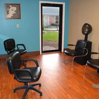 A cozy hair salon interior featuring a waiting area with black chairs and a hair dryer.