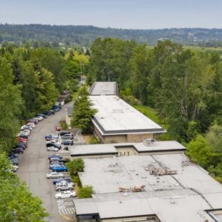 Aerial view of a building surrounded by trees and a parking lot with several cars.
