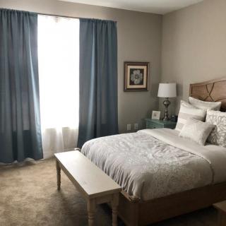 A cozy bedroom with a neatly made bed, blue curtains, and soft lighting.