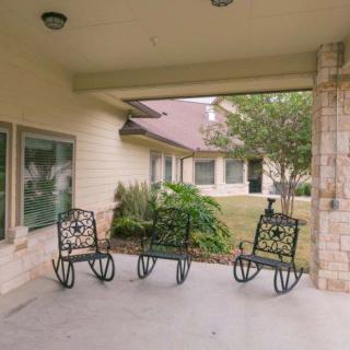 A covered patio area with three decorative metal chairs overlooking a landscaped yard.