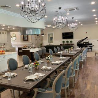 A spacious and elegantly designed dining room featuring a long table set for guests, illuminated by stylish chandeliers.