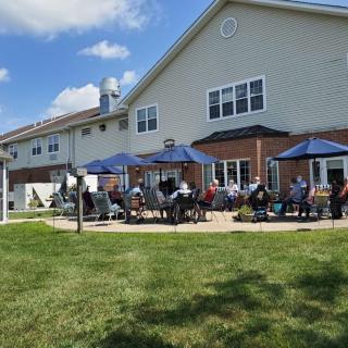 A group of people enjoying a sunny day on a patio with umbrellas outside a large building.