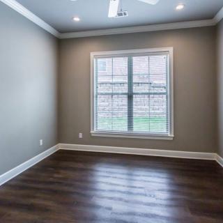 An empty room with hardwood flooring, neutral-colored walls, and a large window allowing natural light to fill the space.