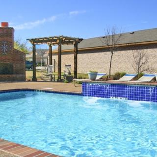 A sunny outdoor swimming pool area with lounge chairs and a pergola.