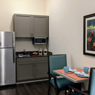 A small kitchen setup with a dining area, featuring a refrigerator, microwave, and neatly arranged tableware.