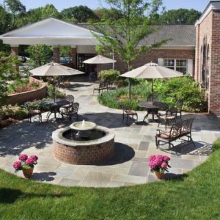 A beautifully landscaped outdoor patio with a central fountain, surrounded by tables and chairs with umbrellas.