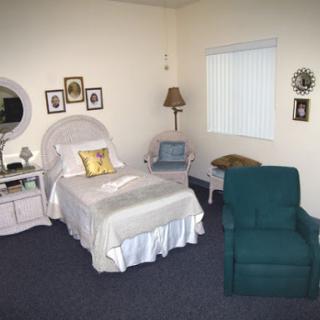 A cozy and well-decorated bedroom featuring a bed, chair, lamp, and wall art.