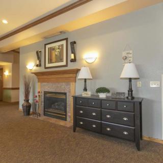A cozy living room interior featuring a fireplace, a chest of drawers with two lamps, and wall artwork.