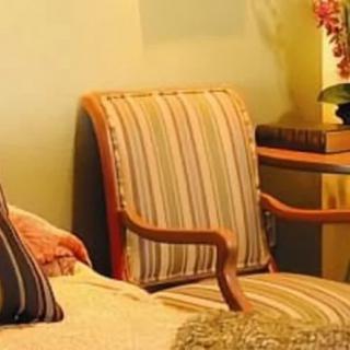 A cozy living room setting featuring a striped upholstered chair with wooden arms and decorative cushions.