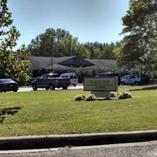 A building with a sign out front, surrounded by parked cars and trees.