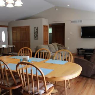 A spacious open-plan dining and living area with a wooden dining table, chairs, and a mounted television.