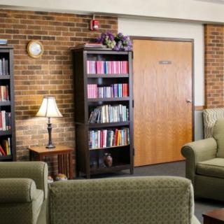 A cozy library reading area with bookshelves, armchairs, and a lamp against a brick wall.