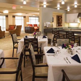 A modern dining area with neatly arranged tables, set with white tablecloths and elegant tableware.