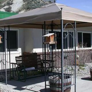 A cozy outdoor patio featuring a metal gazebo with a swing bench and birdhouse under a canopy.